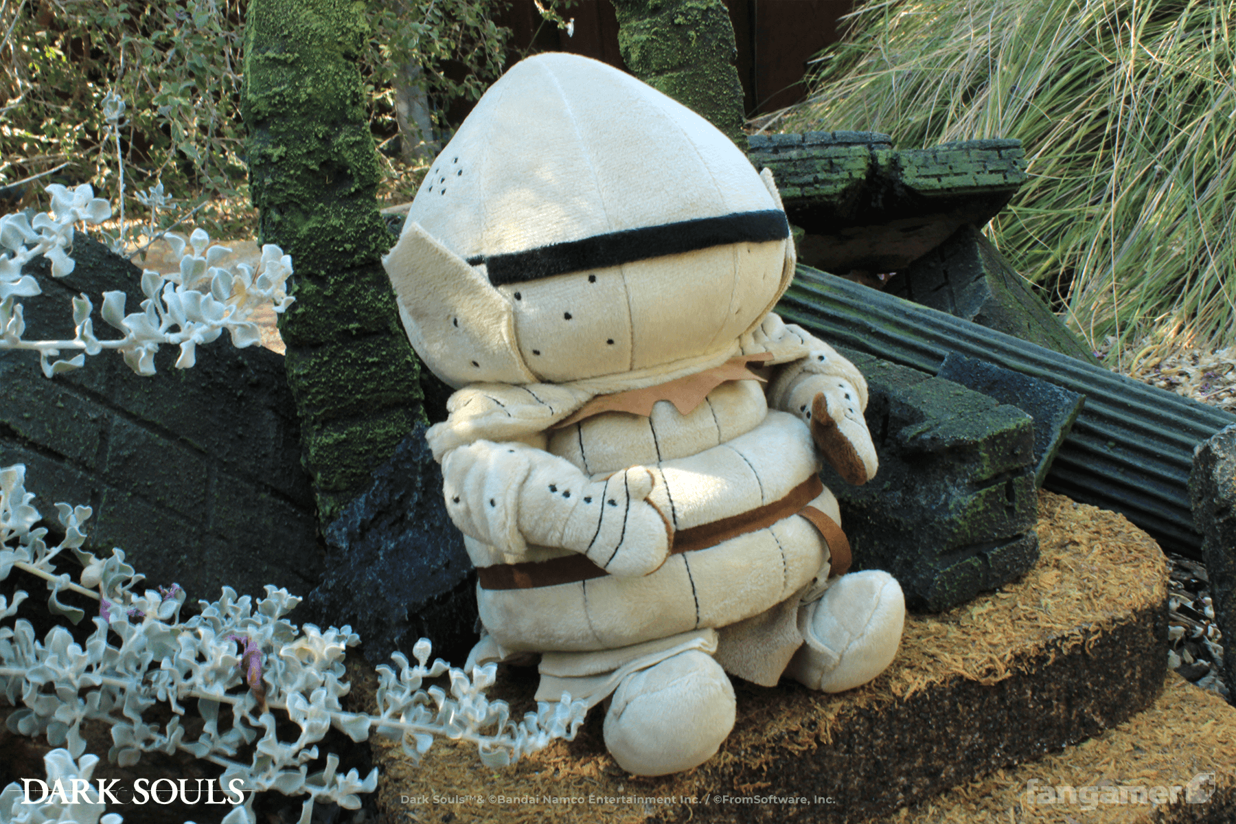 The Siegmeyer plush photographed outdoors at a 3/4 angle, seated next to a flowering bush and miniature ruins. 