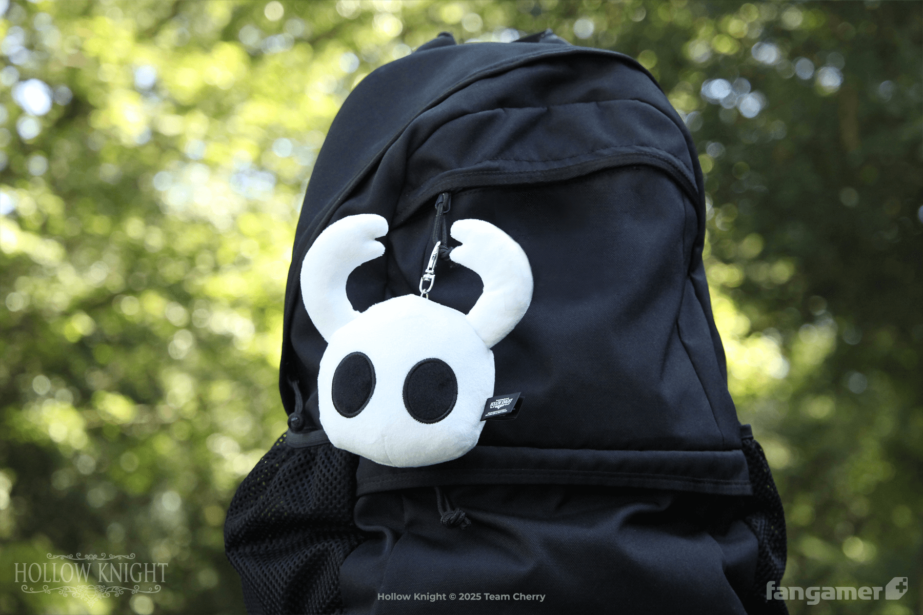 A pouch shaped like the face of The Knight hanging from a black backpack in an outdoor scene. 